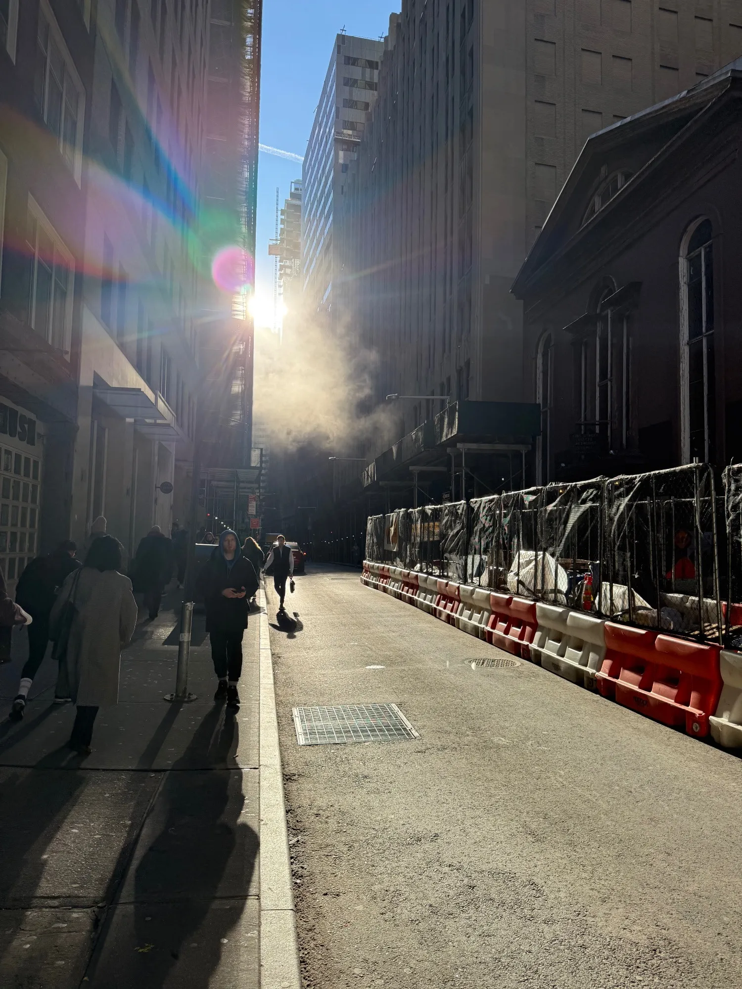 John St. in Manhattan with the sun shining through steam between buildings, casting long shadows