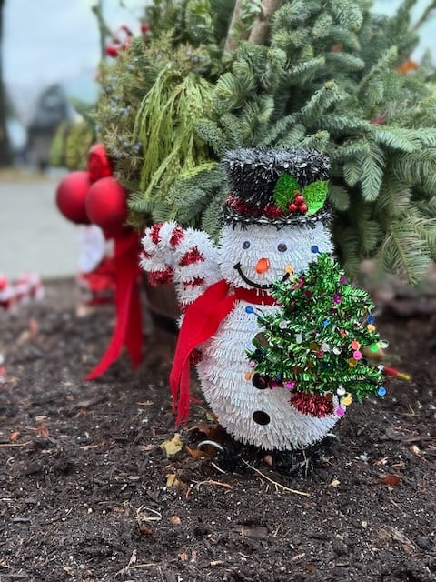 A small snowman decoration at the foot of a small evergreen